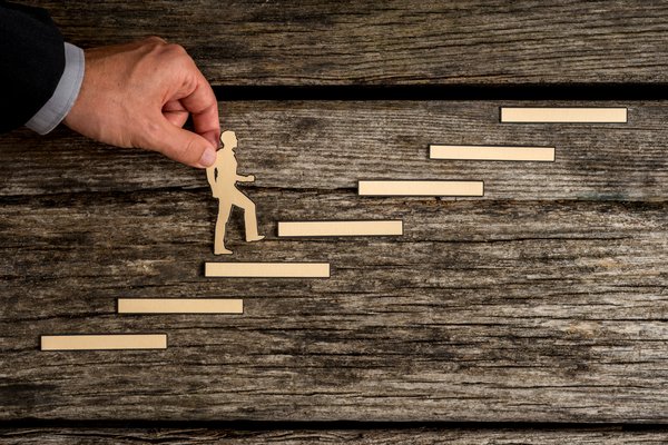 recorte-de-silueta-de-papel-de-un-hombre-y-una-mano-humana-en-traje-de-negocios-ayudandolo-subir-las-escaleras-sobre-madera-rustica